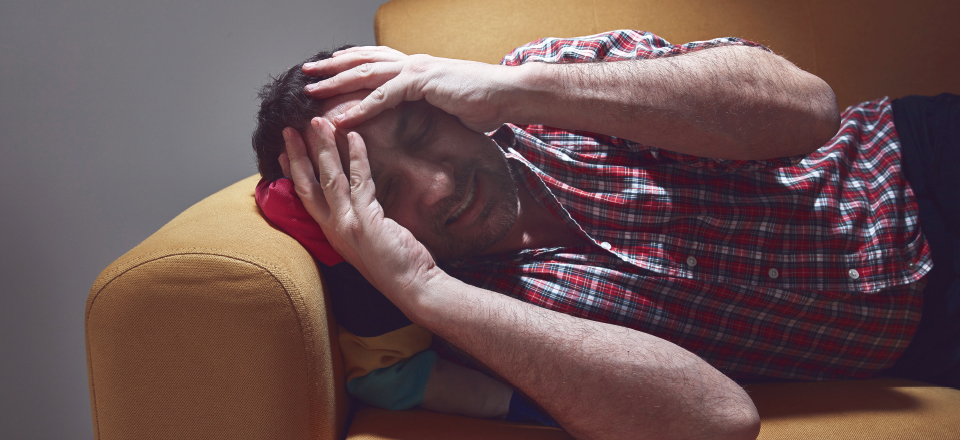 mand med klyngehovedpine - helvedshovedpine ligger på sofaen i smerter, med hænderne på hovedet